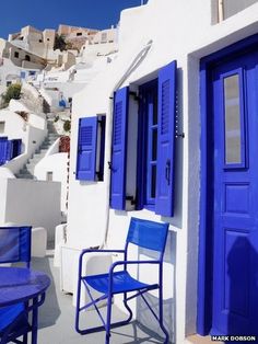 two blue chairs and a table in front of a white building with blue shutters