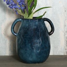 a blue vase filled with purple flowers on top of a wooden table next to a wall