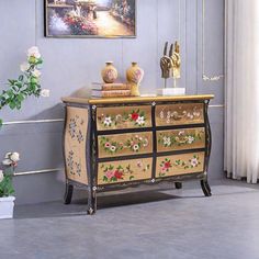 a dresser with flowers painted on it in front of a painting and potted plant