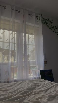 a laptop computer sitting on top of a bed next to a window covered in sheer curtains