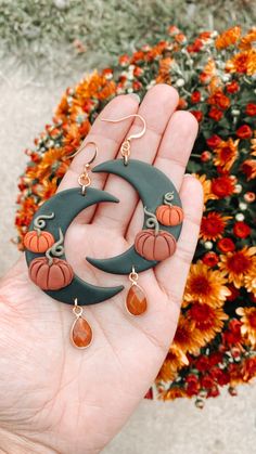 a hand holding a pair of earrings with pumpkins on the moon and tear drops