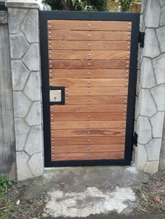 a wooden gate with metal studs on the top and bottom part, in front of a stone wall