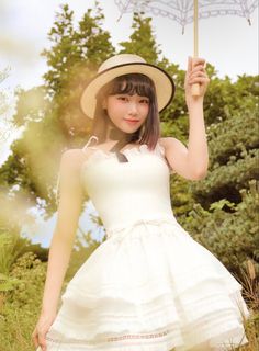 a woman in a white dress and hat holding an umbrella over her head while posing for the camera