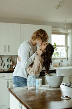 two women kissing in the kitchen while one woman is pouring milk into a bowl on the counter