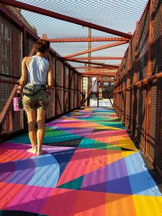 a woman walking across a multicolored walkway in the sun with her back to the camera