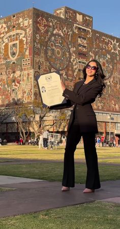 a woman in black suit and sunglasses holding up a piece of paper with images on it