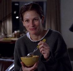 a woman is holding a bowl and spoon in her hand while smiling at the camera