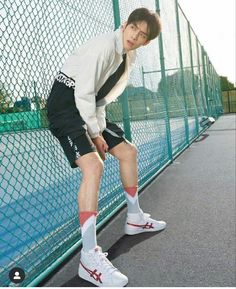 a young man leaning against a fence with his tennis racquet in his hand