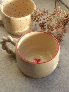 two ceramic cups with handles are sitting on a table next to some flowers and twigs