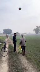 two people standing on a dirt road next to a bike and some balloons in the sky