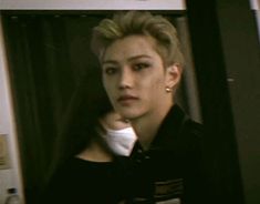 a young man with blonde hair wearing a black shirt and gold earrings looking at the camera