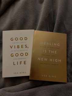 two books sitting on top of a bed next to each other, one is gold and the other is white