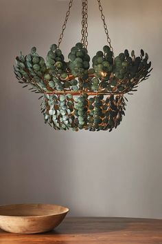 a hanging planter with green plants in it on a wooden table next to a bowl