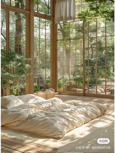 an unmade bed sitting inside of a bedroom next to large glass windows with trees in the background