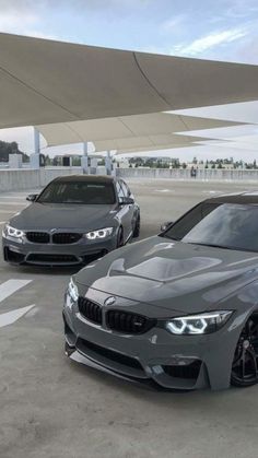 two grey cars parked next to each other in a parking lot with an awning