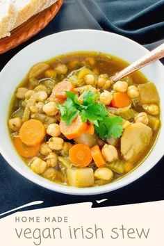 a bowl of soup with carrots, beans and parsley in it next to a piece of bread