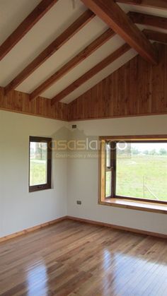 an empty room with wood flooring and two windows on the wall, looking out onto a pasture