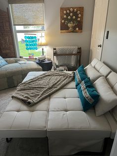 a white bed sitting in a bedroom next to a window covered in blue and green pillows