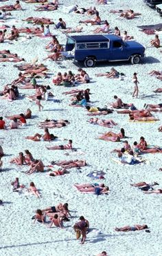 many people are laying on the beach and one car is parked in the sand,