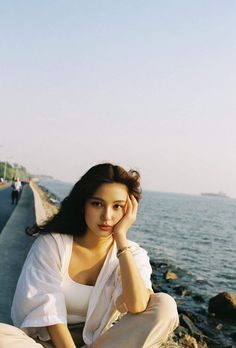 a woman sitting on the edge of a pier next to the ocean with her hand under her head