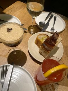 a table topped with plates and bowls filled with food next to glasses of wine on top of a wooden table