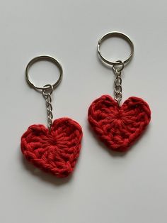 two crocheted heart shaped keychains on a white surface, one is red and the other is silver