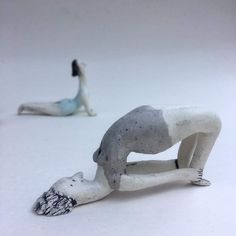 two ceramic figurines sitting on the ground with one laying down and another standing up