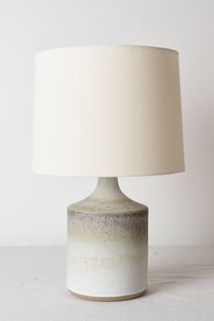 a table lamp with a white shade on the base and a beige drum light bulb