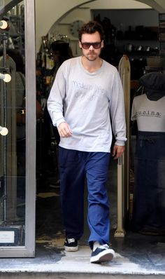 a man walking out of a store with his foot in the glass door and sunglasses on