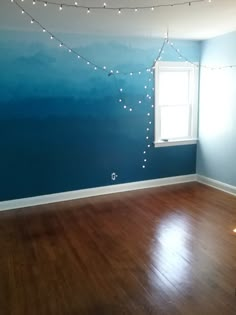 an empty room with wood floors and blue painted walls, string lights hang from the ceiling