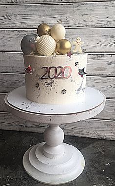 a white cake with gold and silver decorations on it sitting on a pedestal in front of a wooden wall