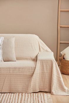 a living room with a white couch covered in a blanket and pillows next to a ladder