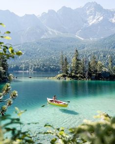 a boat floating on top of a lake surrounded by trees and mountains in the background