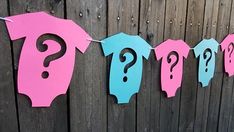 a pink and blue banner with question marks on it hanging from a line next to a wooden fence