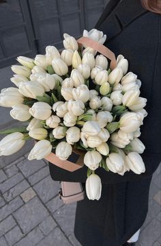 a woman holding a bouquet of white tulips in her hands on the street