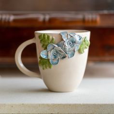 a coffee cup with blue flowers painted on the side and green leaves in the middle