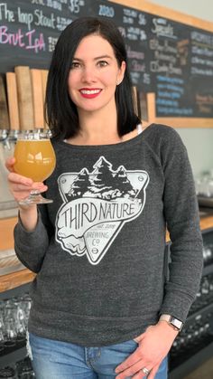 a woman holding a drink in front of a chalkboard with the words third nature on it