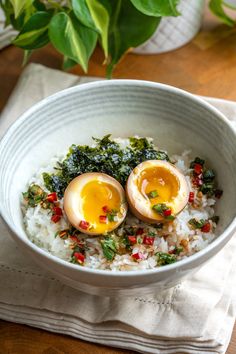 two hard boiled eggs sit on top of rice in a bowl with greens and red peppers