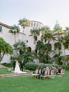 a bride and groom standing in front of a large white building with palm trees on the lawn