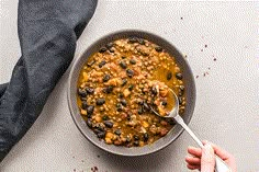 a person holding a spoon in a bowl filled with chili and beans on top of a table