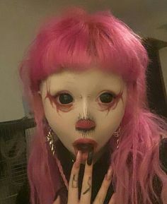 a woman with pink hair and makeup holding her finger up to her mouth