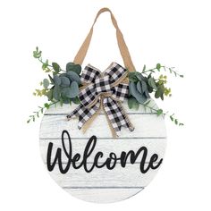 a welcome sign hanging from the side of a wooden plaque with greenery and bow