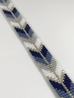 a blue and white beaded bracelet on a white surface with an arrow in the middle