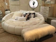 a white round bed with lots of pillows on it in a room filled with furniture