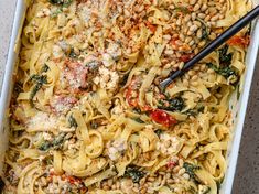 a casserole dish filled with pasta, spinach and other toppings on a table