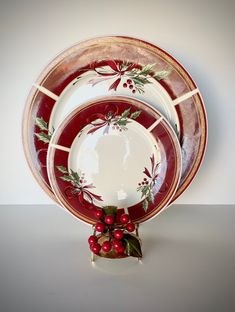 a red and white christmas plate set with holly decorations on the rim, sits in front of a white background