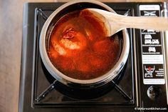 a pot filled with liquid sitting on top of a burner next to a wooden spoon