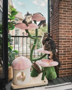 two cats sitting on top of pink flowers in front of a cat tree with stuffed animals