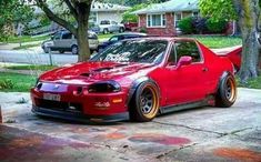 a red car parked in front of a tree on the side of a road next to a house