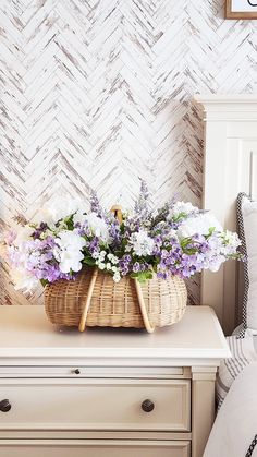 a basket filled with flowers sitting on top of a white dresser next to a clock